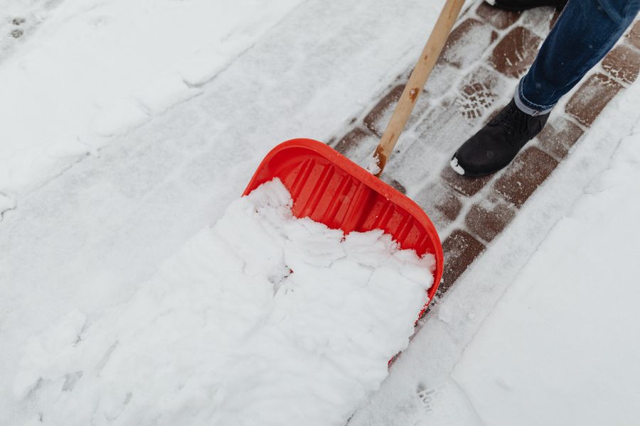 Rote Schneeschaufel räumt Schnee von einem gepflasterten Gehweg